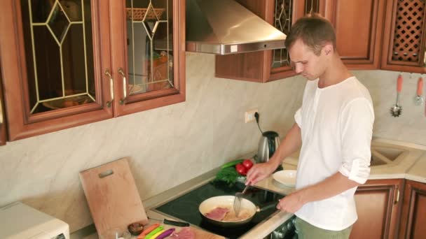 年轻的男人在厨房做饭。准备肉的人。在平底锅上煎 — 图库视频影像