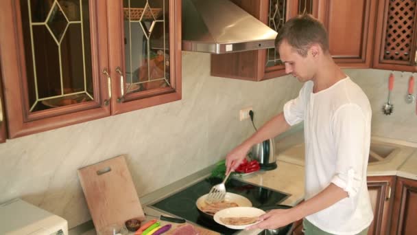 Jovem a cozinhar na cozinha. homem preparando carne. Frite em uma panela — Vídeo de Stock