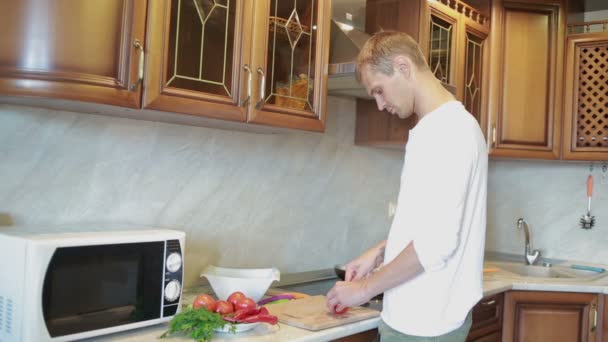 Esposa abraçando seu marido enquanto ele cortando legumes para salada na cozinha — Vídeo de Stock