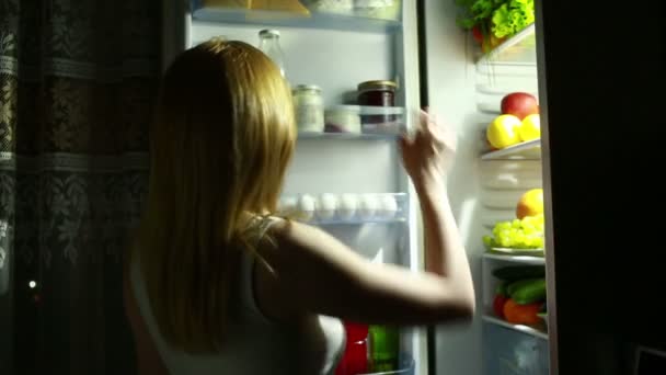 Femme la nuit regardant dans le frigo. fille prend l'orange . — Video