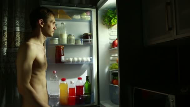 El hombre de la noche se para en el refrigerador abierto. comiendo sándwich. chico hambriento — Vídeo de stock