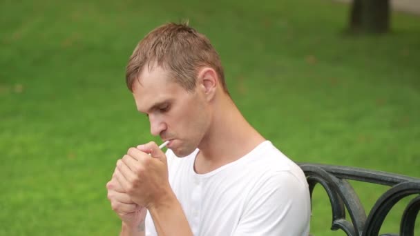 Чоловік палить тонку сигарету в парку — стокове відео