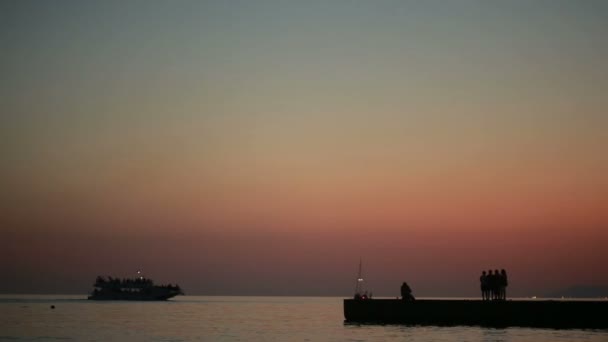 A háttérben a tenger embercsoport. sziluettek a naplemente. Nyáron strand — Stock videók