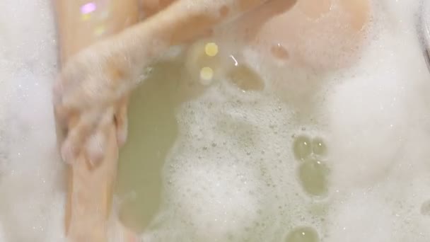 Woman enjoying pleasant bath with foam, washing her leg with a wisp — Stock Video