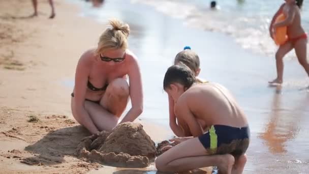 Madre con hijos en la playa. construir un castillo de arena. niño y niña — Vídeos de Stock