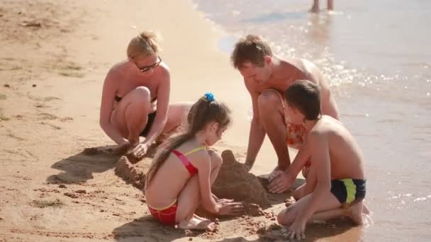 Joven familia caucásica se construye en el castillo de arena de playa — Vídeo de stock