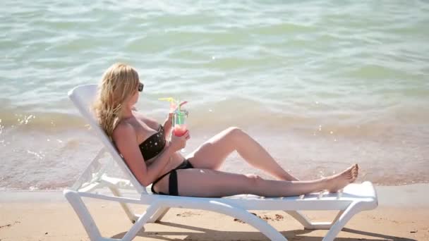 Γυναίκα πίνοντας ένα κοκτέιλ στην παραλία. γυναίκα ηλιοθεραπεία δίπλα στη θάλασσα — Αρχείο Βίντεο