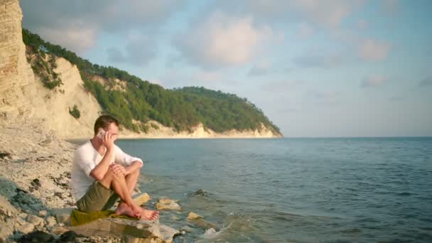男人微笑着坐在沙滩上和浅谈智能手机. — 图库视频影像