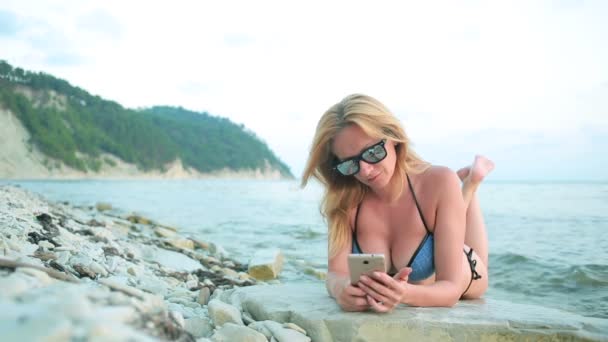 Meisje op het strand met behulp van een smartphone. sexy vrouw in een bikini — Stockvideo