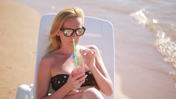 Mujer bebiendo un cóctel en la playa. mujer tomando el sol junto al mar — Vídeo de stock