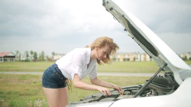 Mulher abre o capô carro quebrado. menina olha para um motor danificado . — Vídeo de Stock