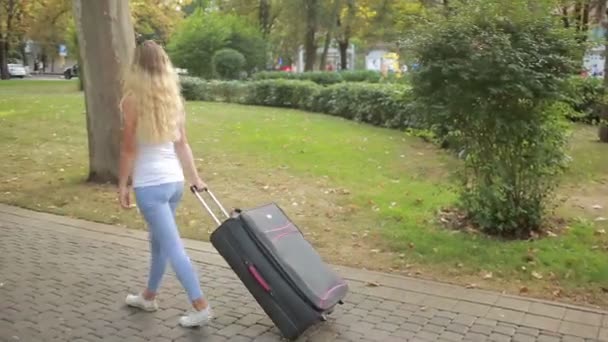 Meisje met een koffer wandelen langs het park. — Stockvideo