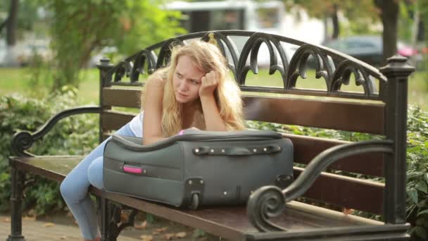 Sad girl sitting on the bench with a suitcase. — Stock Video