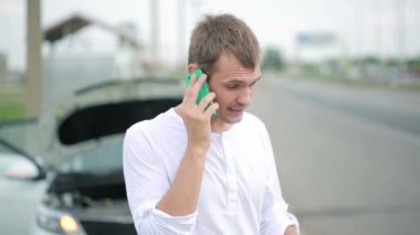 Kırık bir araba ile bir cep telefonuyla konuşan adam