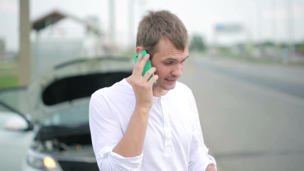 Человек разговаривает по мобильному телефону возле сломанной машины — стоковое видео