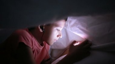 Genç çocuk bir cep telefonu veya bir yatakta smartphone ile oynamak. gece