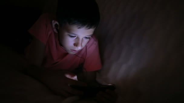 Niño jugando con un teléfono celular o smartphone en una cama. noche — Vídeos de Stock