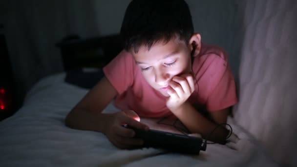 少年は携帯電話やスマート フォン、ベッドの上で遊んでいます。夜 — ストック動画