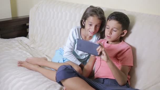 Підлітки використовують смартфон з навушниками. брат і сестра з телефоном — стокове відео