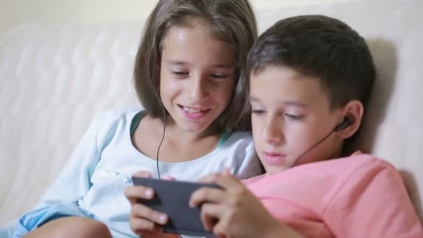 Młodzieży przy użyciu smartfona z słuchawki. brat i siostra z telefonem — Wideo stockowe
