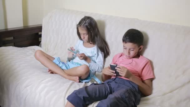 男の子と女の子は、あなたの携帯電話とソファの上に座って。オンライン ゲーム — ストック動画
