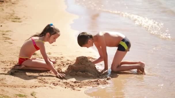 Barn. pojke och flicka som leker med sand på stranden. bygga ett sandslott — Stockvideo