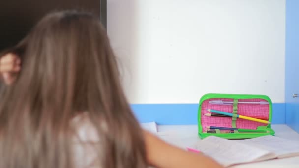 Schoolgirl doing homework at the table leafs through book. Girl makes lessons — Stock Video