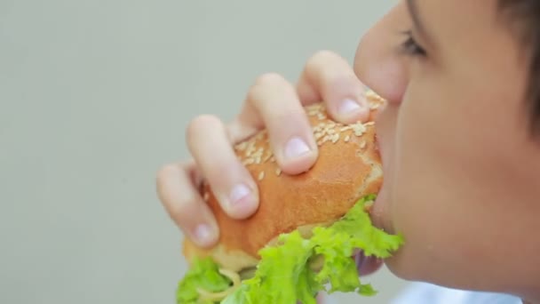 Chico al aire libre comiendo una hamburguesa. niño comiendo un sándwich en la calle — Vídeo de stock