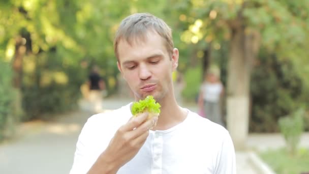 Красивый мужчина ест бутерброд на улице — стоковое видео