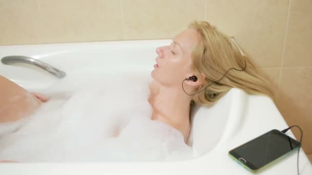 Beautiful woman taking a bath and listening to music on headphones. cell phone — Stock Video