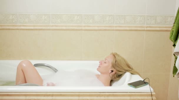 Красива жінка приймає ванну і слухає музику на навушниках. мобільний телефон — стокове відео