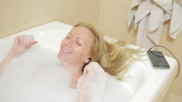 Hermosa mujer tomando un baño y escuchando música en los auriculares. teléfono celular — Vídeos de Stock