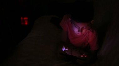 Genç çocuk bir cep telefonu veya bir yatakta smartphone ile oynamak. gece