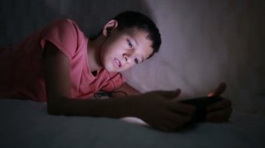 Genç çocuk bir cep telefonu veya bir yatakta smartphone ile oynamak. gece