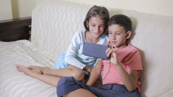 Adolescentes usando smartphone con auriculares. hermano y hermana con un teléfono — Vídeo de stock