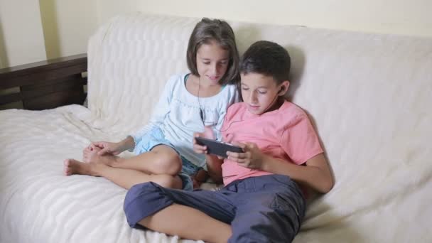 Підлітки використовують смартфон з навушниками. брат і сестра з телефоном — стокове відео