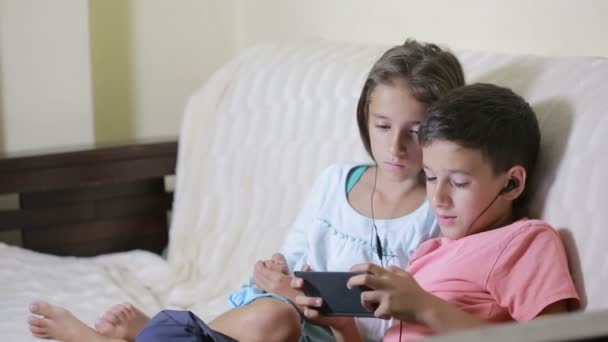 Adolescentes usando smartphone com fones de ouvido. irmão e irmã com um telefone — Vídeo de Stock