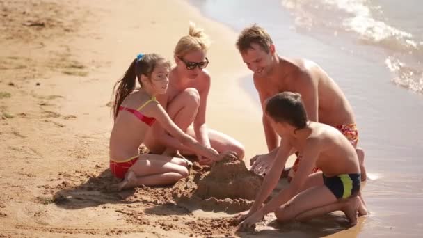 Jovem família caucasiana é construído na praia castelo de areia — Vídeo de Stock