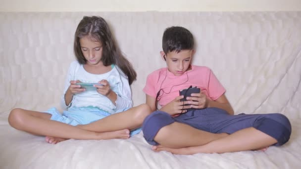 Хлопчик і дівчинка сидять на дивані з телефоном. Онлайн ігри — стокове відео