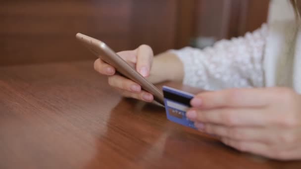 Mujer hace una compra usando un teléfono inteligente y una tarjeta bancaria . — Vídeo de stock