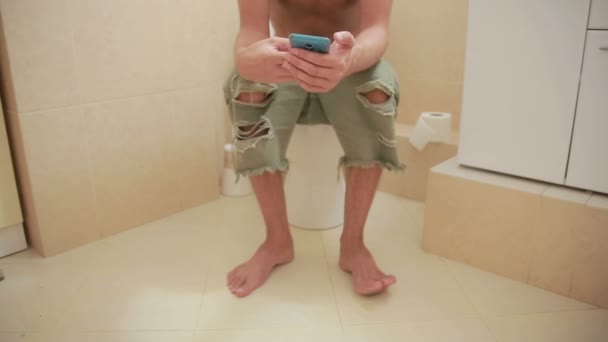 Homem sentado em um banheiro e olha no telefone celular — Vídeo de Stock