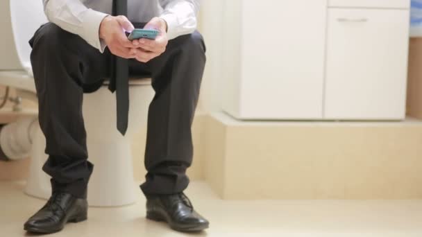 Male businessman watches the news on the phone sitting on the toilet — Stock Video