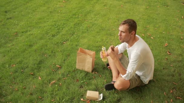 Oběd na louce chlap. muž jí sendvič na trávníku a pití šťávy. — Stock video