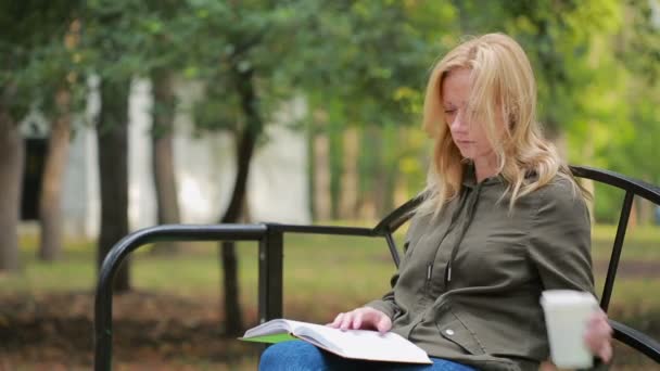 Blonde vrouw leesboek op Brench in de herfst Park. warme koffie of thee drinken — Stockvideo