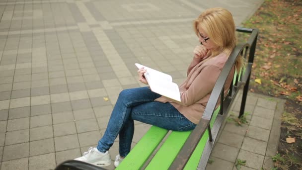 Ξανθιά γυναίκα ανάγνωση βιβλίων σε Brench σε πάρκο φθινόπωρο. — Αρχείο Βίντεο