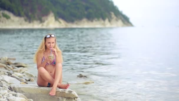 Mädchen im Bikini trinken Saft durch einen Strohhalm. Frau am Meer. — Stockvideo