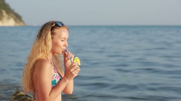 Meisje in bikini drink SAP met een rietje. vrouw aan de zee. — Stockvideo