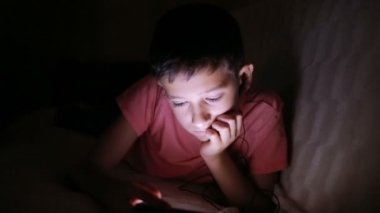 Genç çocuk bir cep telefonu veya bir yatakta smartphone ile oynamak. gece