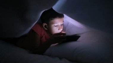 Çocuk bir cep telefonu veya bir yatakta smartphone ile oynamak. bir battaniyenin altında gizleme