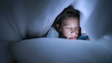 Geceleri bir cep telefonu kullanan küçük kız. bir battaniyenin altında gizleme